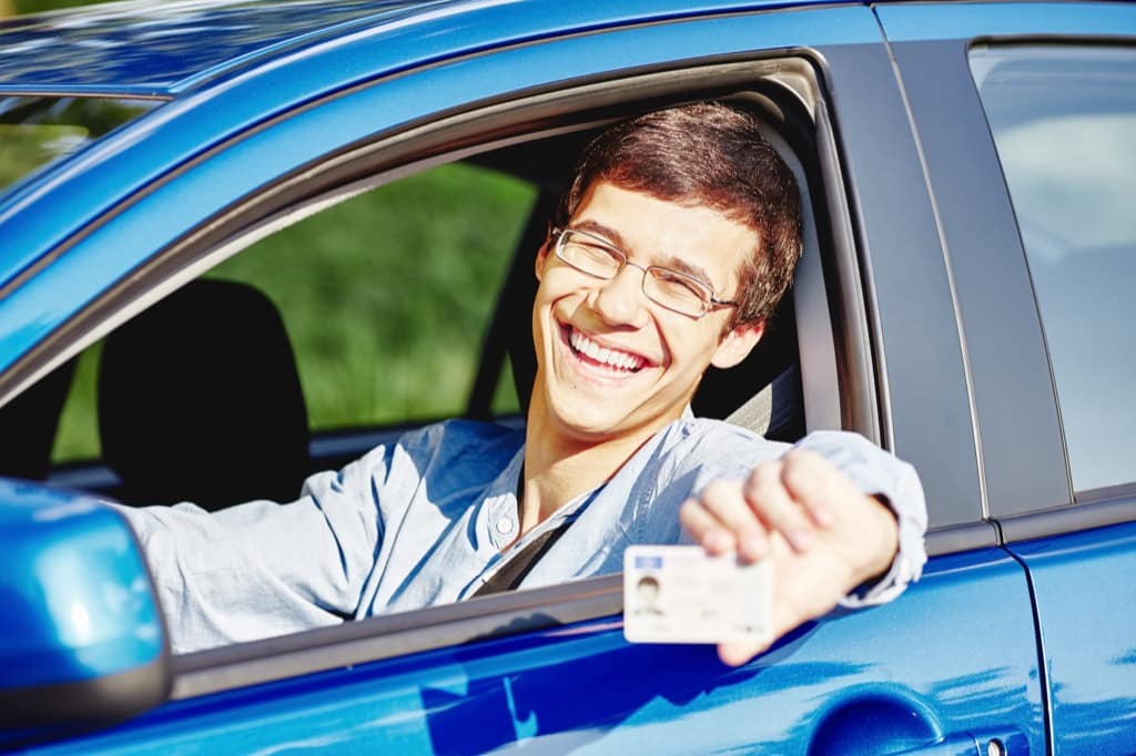 Young man sitting in a car and holding up his driver's license