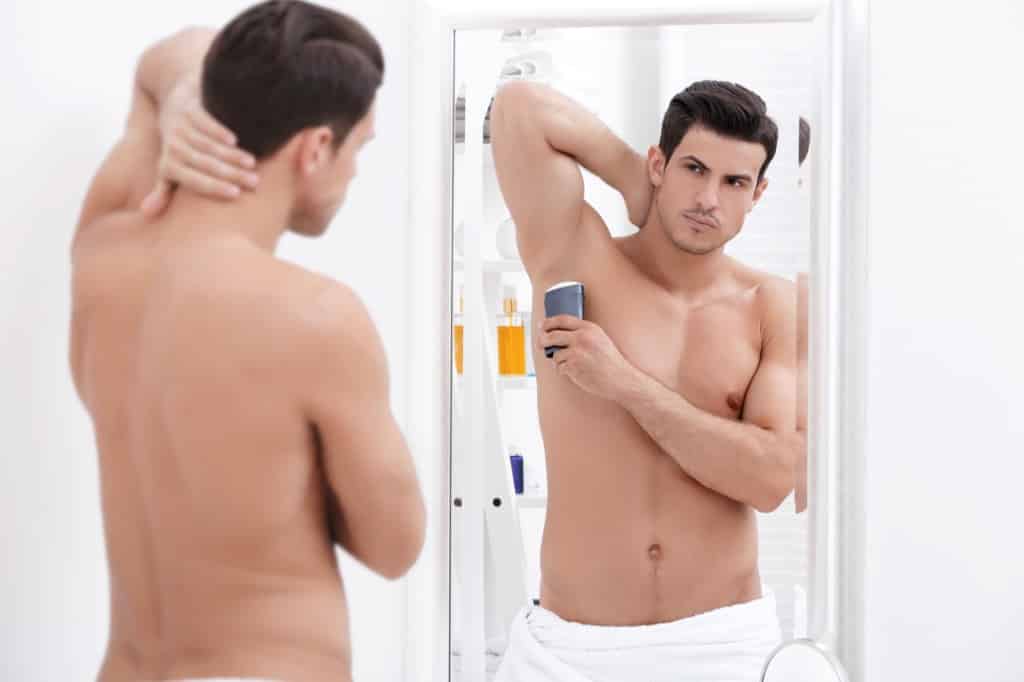 Man putting on deodorant in mirror